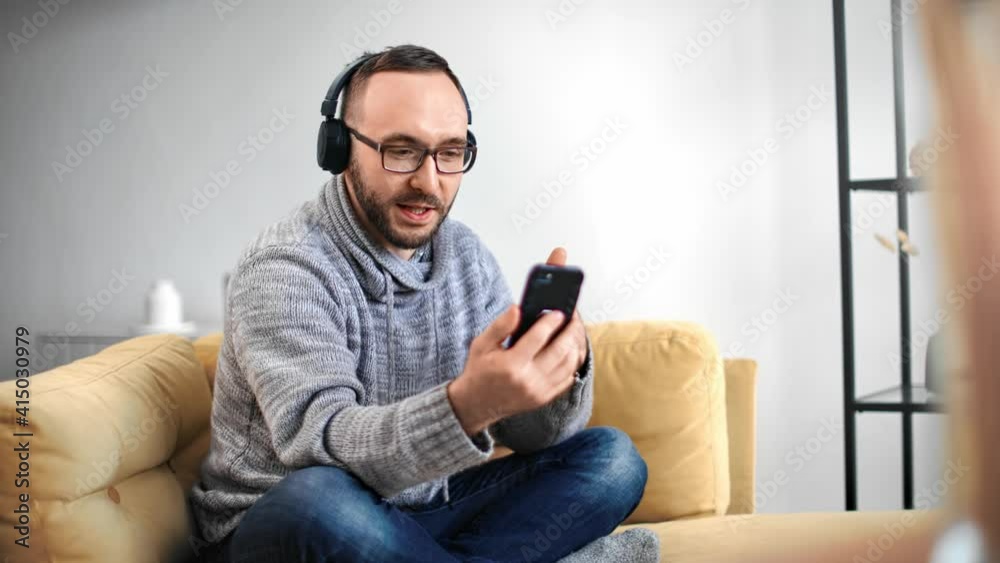 Casual guy in headphones smiling talking online video call smartphone. Shot with RED camera in 4K Casual guy in headphones smiling talking online video call smartphone. Shot with RED camera in 4K