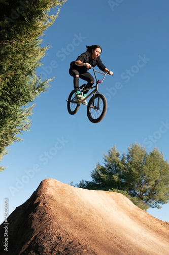 Fototapete Caucasian white with long hair boy jumping with BMX bike on a mountain in the fi