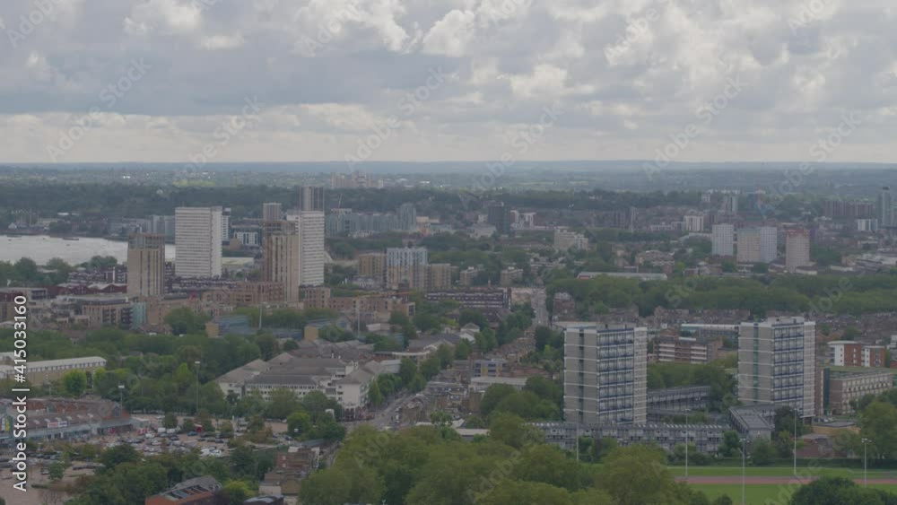 Aerial drone view across suburban London with residential housing and tower blocks and green spaces and trees on a clear and cloudy day
