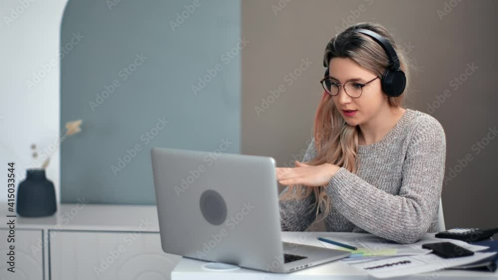 Modern freelancer woman in headphones talking online video call laptop. Medium shot on RED camera Modern freelancer woman in headphones talking online video call laptop. Medium shot on RED camera