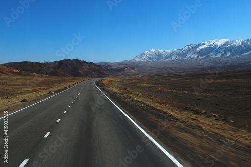 Alpine road in motion among the Alatau mountain ranges and a wide valley in Altyn-Emel national park, snow-covered ridge, clear sky, spring, sunny