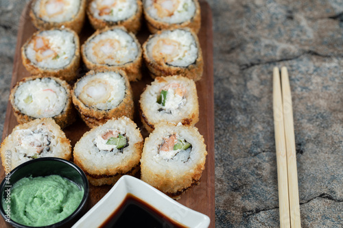 Fried hot sushi rolls with cream cheese, wasabi and soy sauce on a wooden board