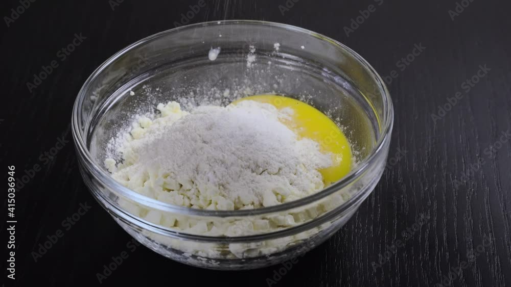 The cook adds flour, a broken egg in a plate with cottage cheese, for further preparation of cheesecakes or other dishes. The cook adds flour, a broken egg in a plate with cottage cheese, for further preparation of cheesecakes or other dishes.