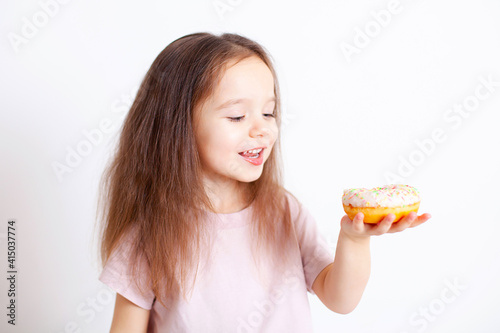 The girl is going to bite off the doughnut. Tasty and sweet. Harmful food. Healthy food. Eating a child. Child health. Fast food