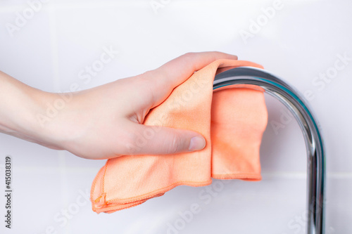 The hand wipes the faucet with a napkin. Close-up in light colors. House cleaning. Cleanliness. Eco-cleaning. 