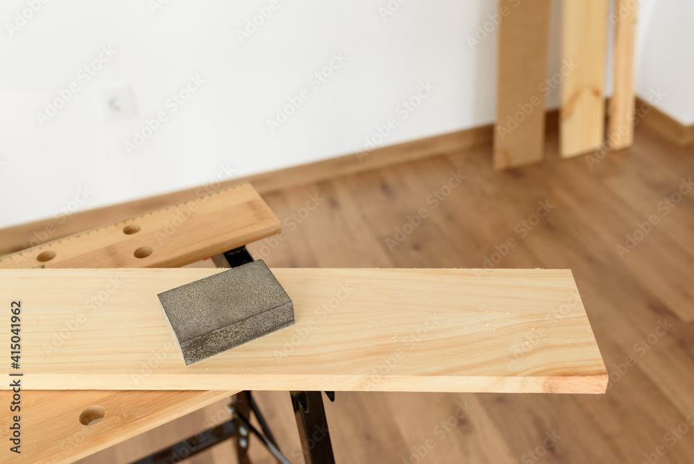 Close up shot of a wooden sandpaper on a workbench with a woman working in the background.