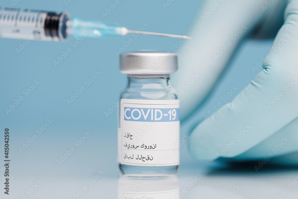 Closeup of crop unrecognizable doctor in gloves filling syringe with vaccine from coronavirus in glass vial on blue background Closeup of crop unrecognizable doctor in gloves filling syringe with vaccine from coronavirus in glass vial on blue background