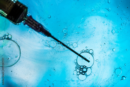 Closeup of needle of syringe filled with vaccine from virus injected in cell on blurred background photo