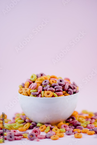 From above pile of colorful cereal rings in bowl prepared for breakfast placed on violet table in studio