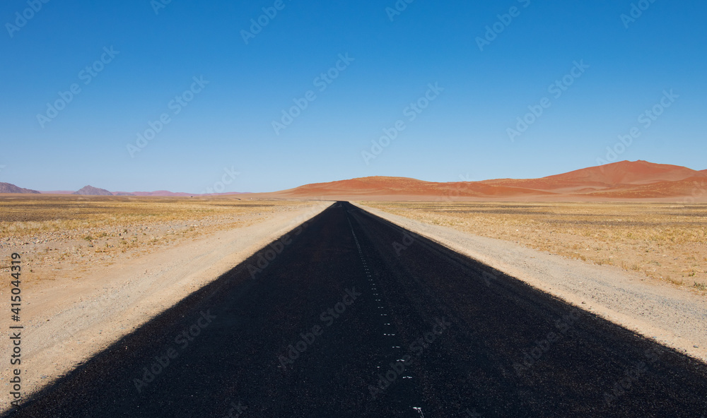 endless paved road.  View along a black paved road from Sesriem to Sossussvlei in Naukluft Park, Namibia. Red dunes at the horizon.