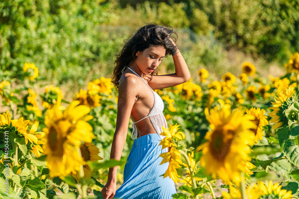 Side view of slim ethnic female standing in field with blooming sunflowers on sunny day in summer Side view of slim ethnic female standing in field with blooming sunflowers on sunny day in summer