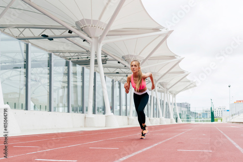 Attractive young sportswoman in sportswear sprinting on track field photo