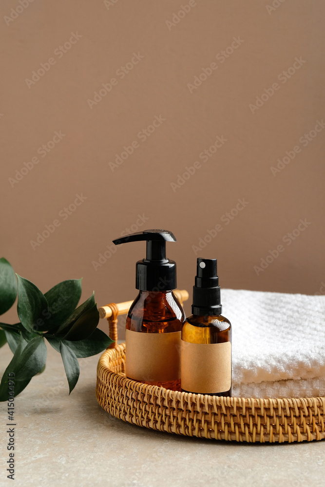 Rattan basket with natural organic SPA cosmetic products and towel, green leaves on table in bathroom. Herbal skincare beauty products design, branding.