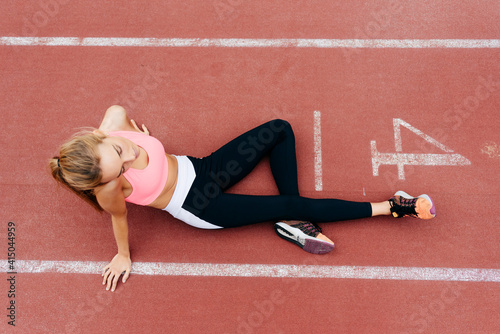 From above blonde young sportswoman sitting on the floor resting on tracking field