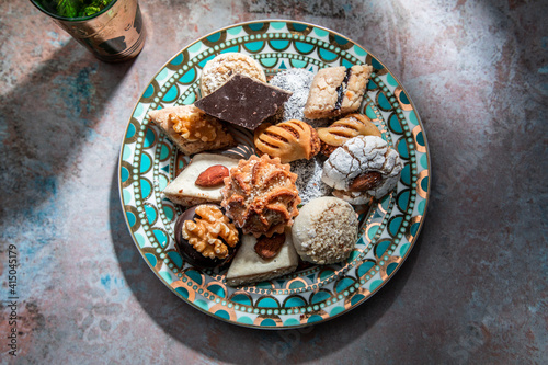 From above of baklava and biscuits with Moroccan peppermint tea near knife and fork placed on table decorated with mint leaves