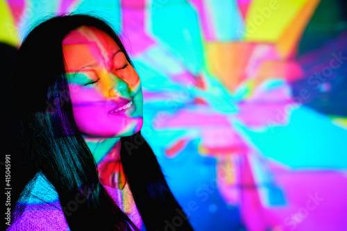Stock photo of cool asian woman with colorful lights in her face closing her eyes.
