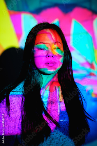 Stock photo of cool asian woman with colorful lights in her face closing her eyes.