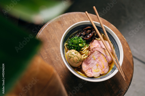 Top view of delicious traditional ramen soup in bowl with chopsticks served on round table photo