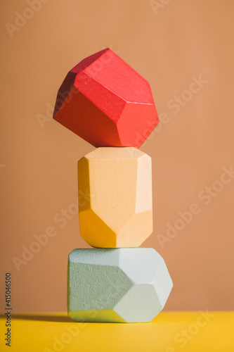 Wooden blocks in shapes of gems of various colors stacked on beige background in studio