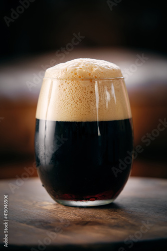 Dark craft beer with foam in glass served on round table in bar