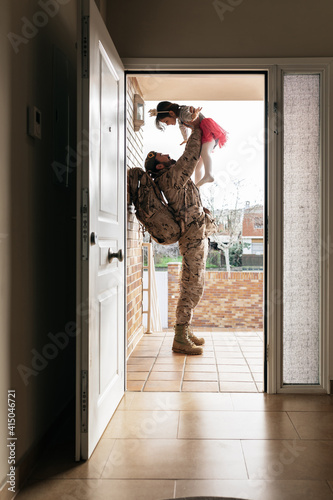 Side view of military man tossing little girl while standing at doorway of house after homecoming photo