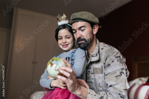 From below of positive soldier talking to daughter and pointing at place at globe before going to serve in army photo