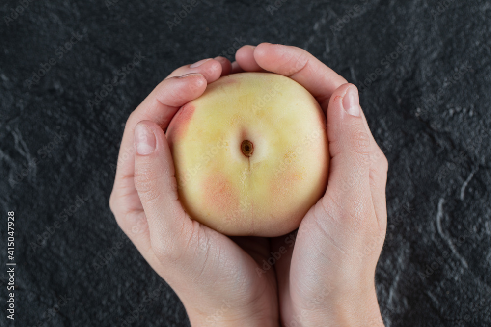 A person holding a yellow peach in the palm A person holding a yellow peach in the palm