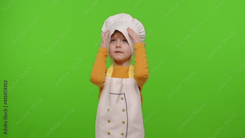 Child girl kid dressed as professional cook chef smiling, crosses arms and looks intently at camera on chroma key background. Nutrition, cooking school, education, food. Fun and humor. Copy-space Child girl kid dressed as professional cook chef smiling, crosses arms and looks intently at camera on chroma key background. Nutrition, cooking school, education, food. Fun and humor. Copy-space