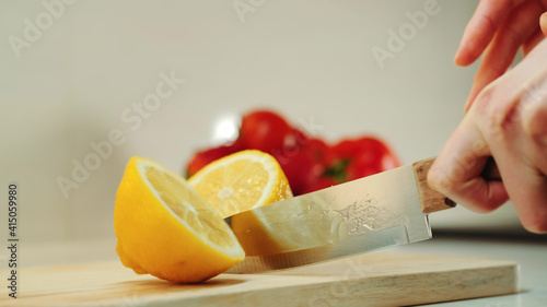 Hands with knife cutting lemon on the kitchen board. Close up shot photo