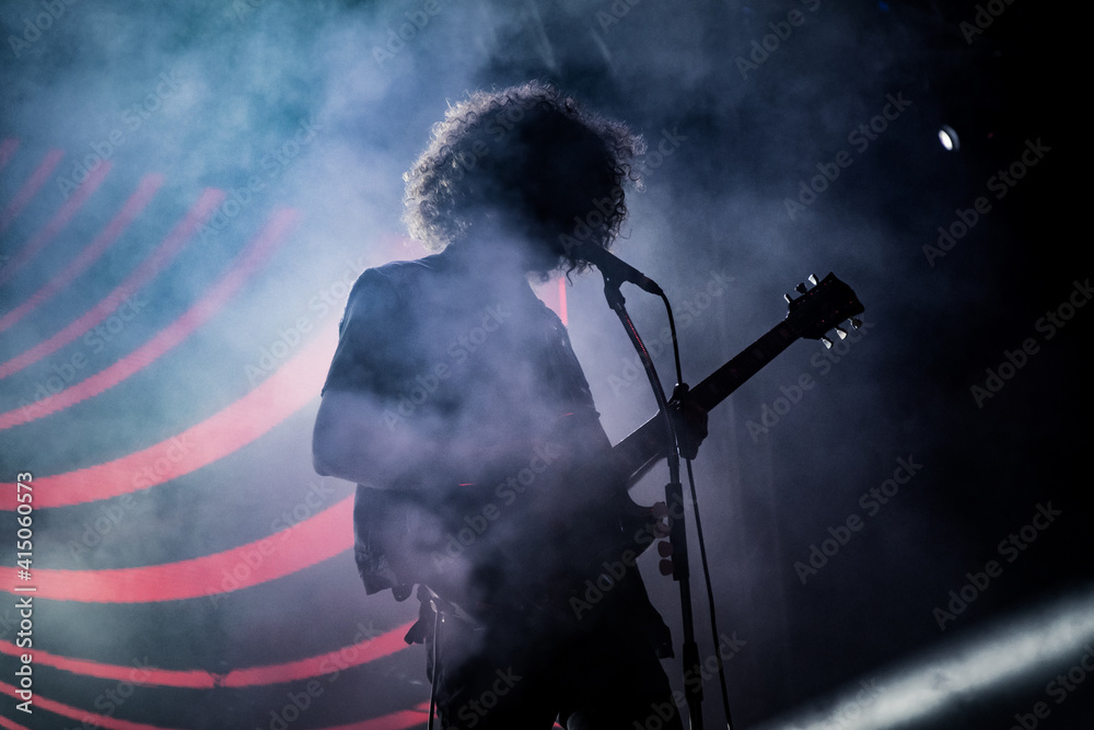 Guitarist stands silhouetted playing solo on stage with smoke, light beams and LED pattern 