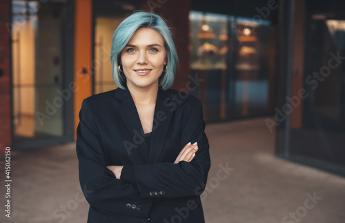 Front view photo of a caucasian lady with blue hair posing with crossed hand and smile at camera