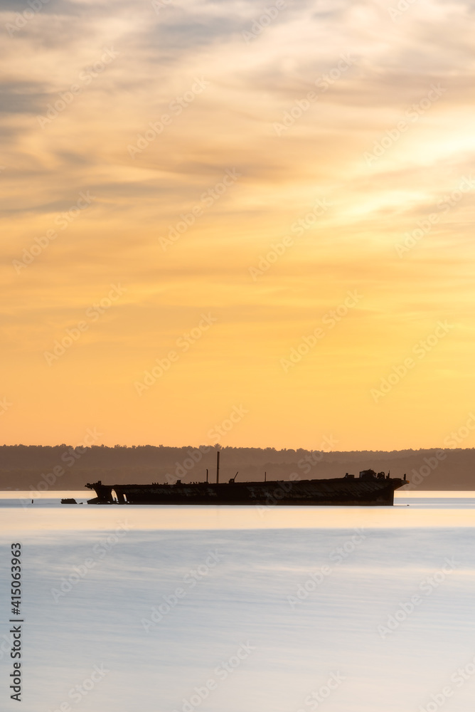 The silhouette of the SS Accomac in Mallows Bay during golden evening light on the Potomac River.