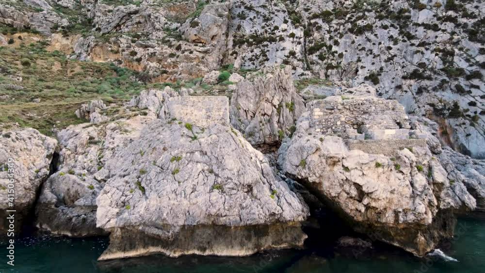 Drone flies backwards through rocks in a rough environment above the ocean and crystal clear water. Drone flies backwards through rocks in a rough environment above the ocean and crystal clear water.