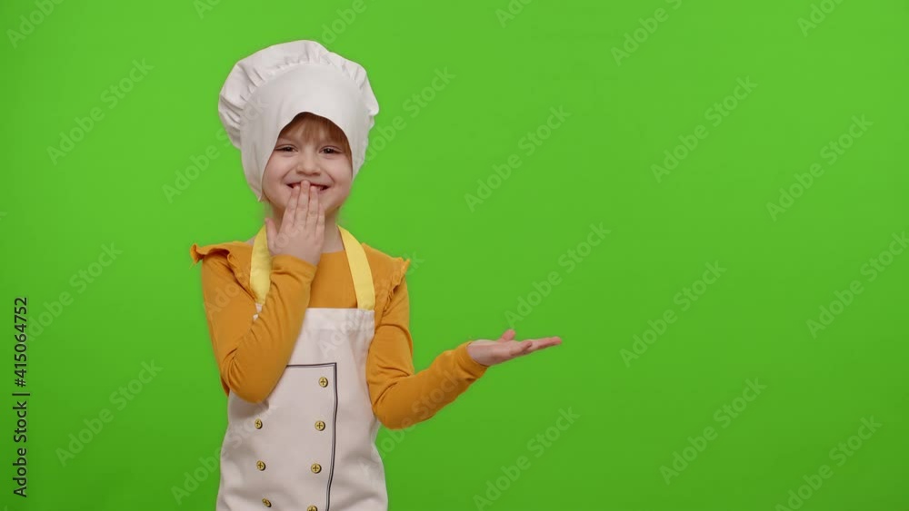 Funny preschooler child girl dressed cook chef baker in apron and hat pointing at right on blank space on chroma key background. Place for your advertisement logo. Cooking school, children education Funny preschooler child girl dressed cook chef baker in apron and hat pointing at right on blank space on chroma key background. Place for your advertisement logo. Cooking school, children education