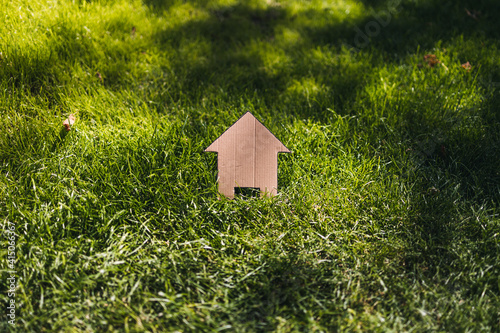 green home and eco-friendly construction, house icon on green grass lawn under the sun with garden bokeh photo