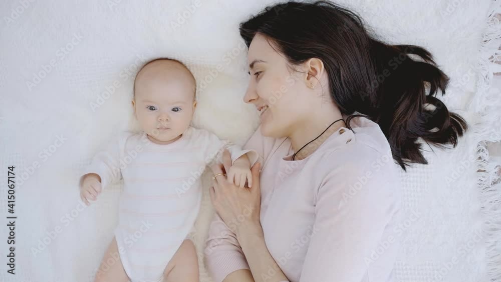 Happy mom and newborn baby, boy or girl lie on the bed and dangle legs and arms Happy mom and newborn baby, boy or girl lie on the bed and dangle legs and arms