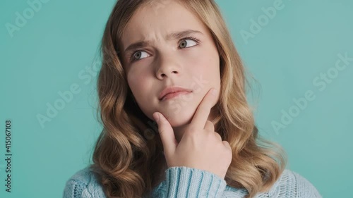 Close up pensive blond teenager girl keeping hand on chin thinking about something isolated on blue background. Face expression