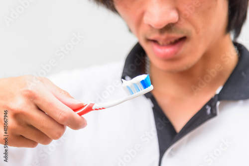 The asian man show the toothbrush with toothpaste in his hand