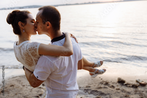 A man holds a woman in his arms and kisses. A young girl hugs the man tenderly by the neck. A loving couple kissing. People stand by the river. High quality photo