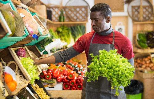 Focused African man working at farmer market, putting fresh fruits and vegetables on showcase..