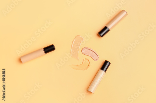 Bottles of makeup foundation and samples on color background