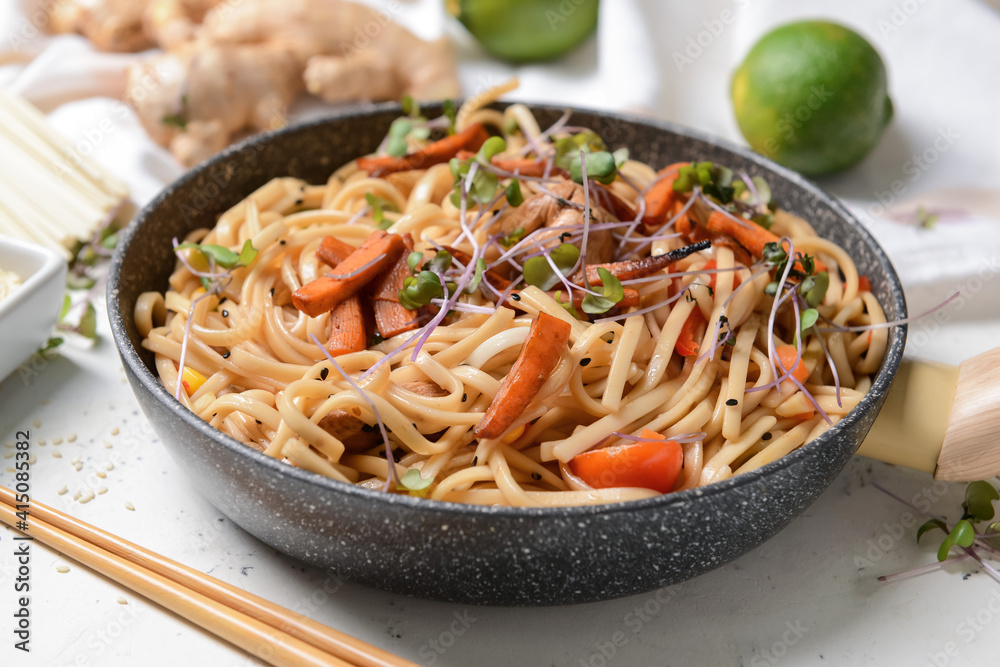 Frying pan with noodles and meat on light background