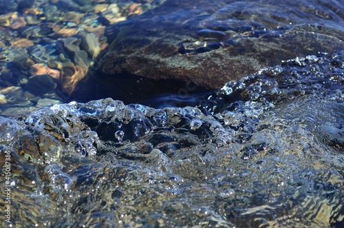 beautiful ripples on river flow over colorful stones in summer sunshine