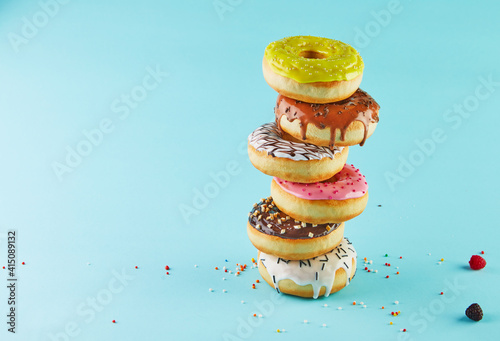 Multicolored donuts with icing and sprinkling stacked in a stack on a blue background