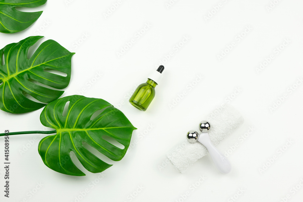 A CBD green oil, face roller, white cotton towel and green leaves of monstera lie on a white table A CBD green oil, face roller, white cotton towel and green leaves of monstera lie on a white table