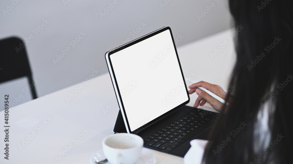 Cropped shot of young woman office worker holding stylus pen and working with computer tablet at white office desk. Cropped shot of young woman office worker holding stylus pen and working with computer tablet at white office desk.