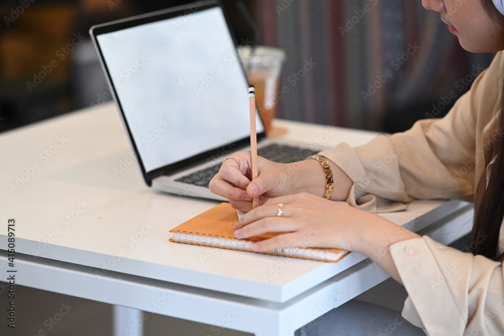Cropped shot of businesswoman writing something on notebook and working with computer laptop at office desk. Cropped shot of businesswoman writing something on notebook and working with computer laptop at office desk.