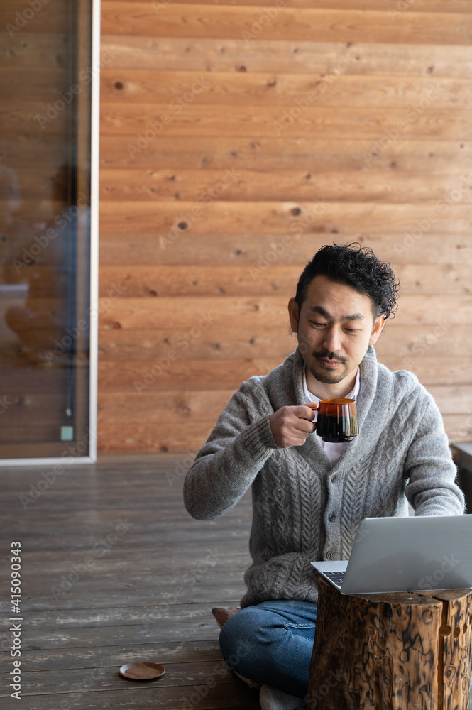 お洒落な木造の部屋でコーヒーを飲みながら株価をチェックしている日本人男性 コピースペースあり 縦 お洒落な木造の部屋でコーヒーを飲みながら株価をチェックしている日本人男性 コピースペースあり 縦