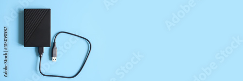 external hard drive black color with connection cable on blue background. banner