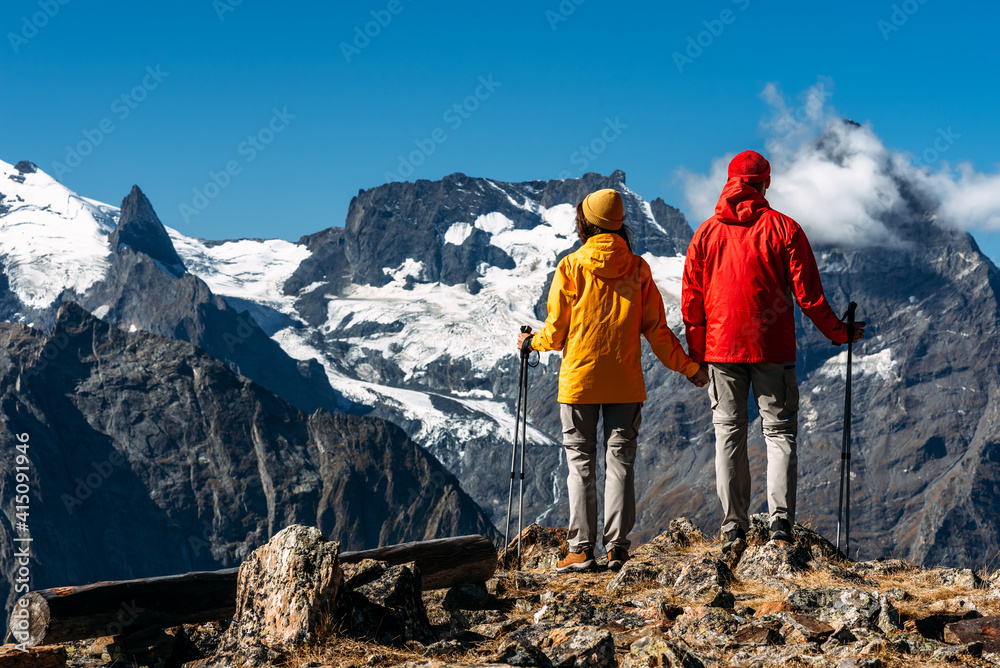 Young couple doing Nordic walking in the mountains, rear view. An active couple is engaged in Hiking. A young couple is engaged in tracking. Trekking and Nordic walking. Hiking. Copy space